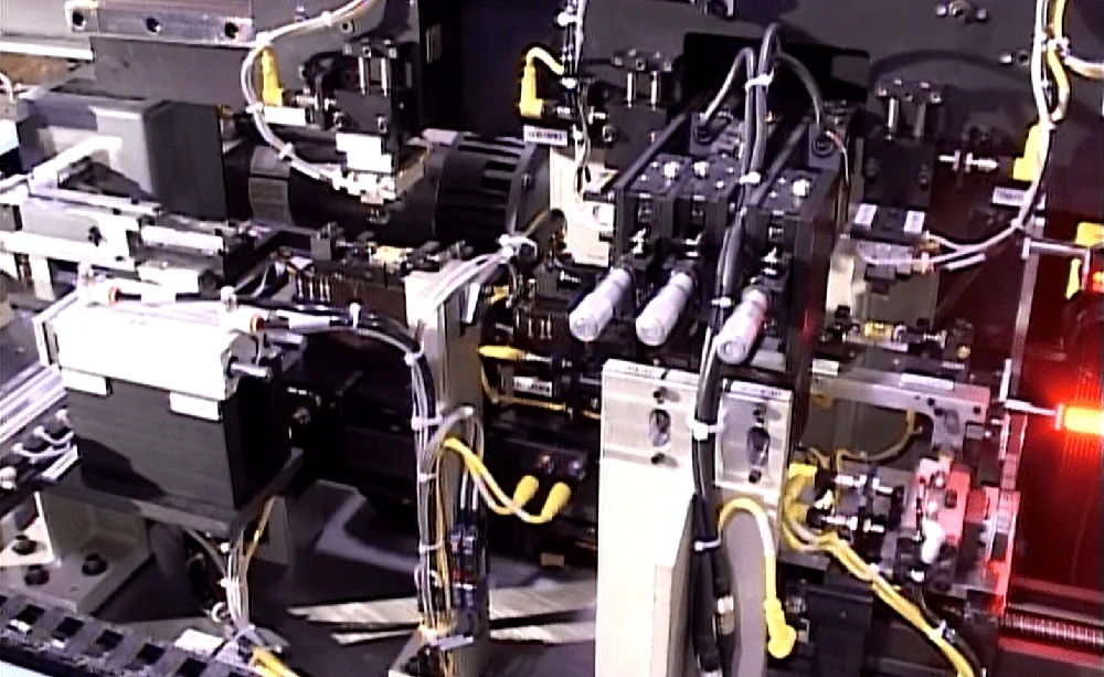 Close-up of black tooling on a connector assembly machine with a red indicator light